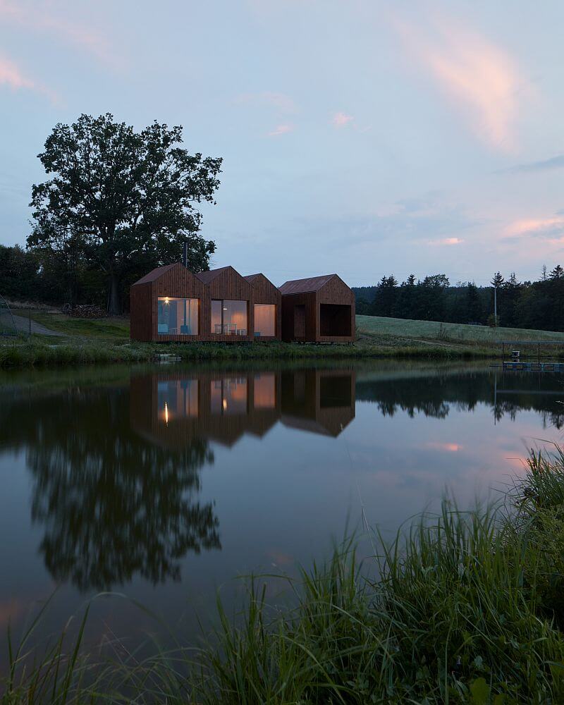 drevena-chata-u-rybnika-vysocina-exterier-velkoformatova-okna-drevena-fasada-hladina-rybnika-odraz-na-hladine-vecer