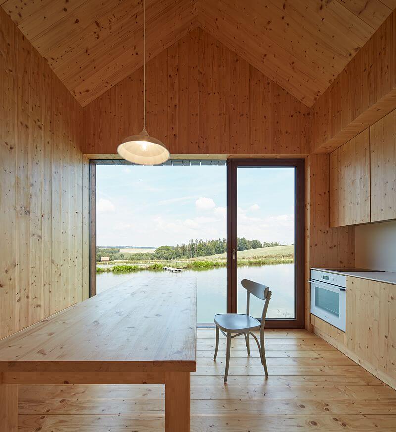 drevena-chata-u-rybnika-vysocina-interier-kuchynsky-kout-jidelni-stul-drevo-v-interieru-velkoformatove-okno-vyhled-na-rybnik