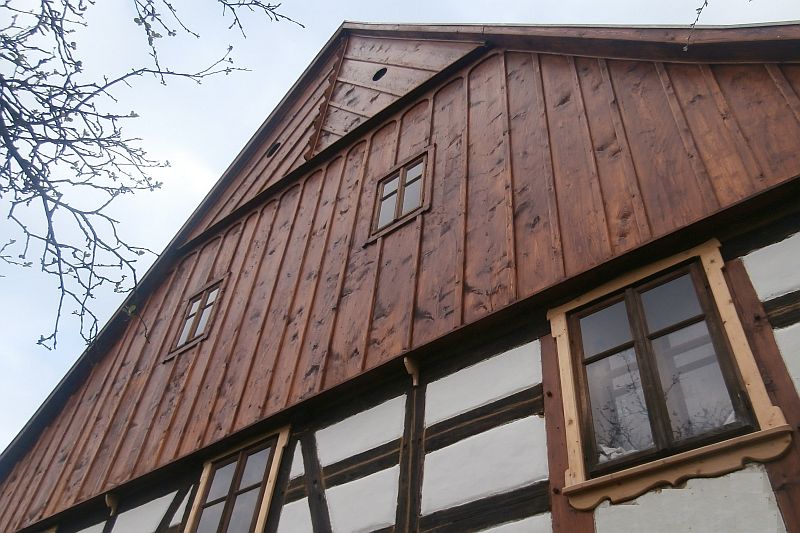 Obnoven&aacute; lomenice hlavn&iacute;ho &scaron;t&iacute;tu tvořen&aacute; různě &scaron;irok&yacute;mi prkny a vyřez&aacute;van&yacute;mi li&scaron;tami na podst&aacute;vkov&eacute;m domě.