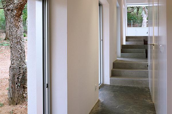 Dům ve svahu - interi&eacute;r chodby se schody a velk&yacute;mi okny.