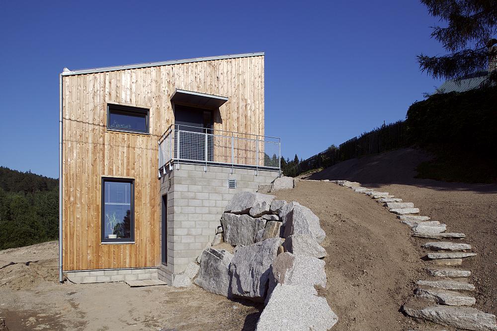 Dřevostavba ve svahu s cestou a vydl&aacute;žděn&yacute;mi patn&iacute;ky.