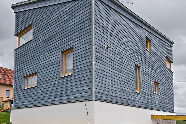 Dřevostavba ve svahu s netradičn&iacute; barvou smrkov&eacute; fas&aacute;dy.