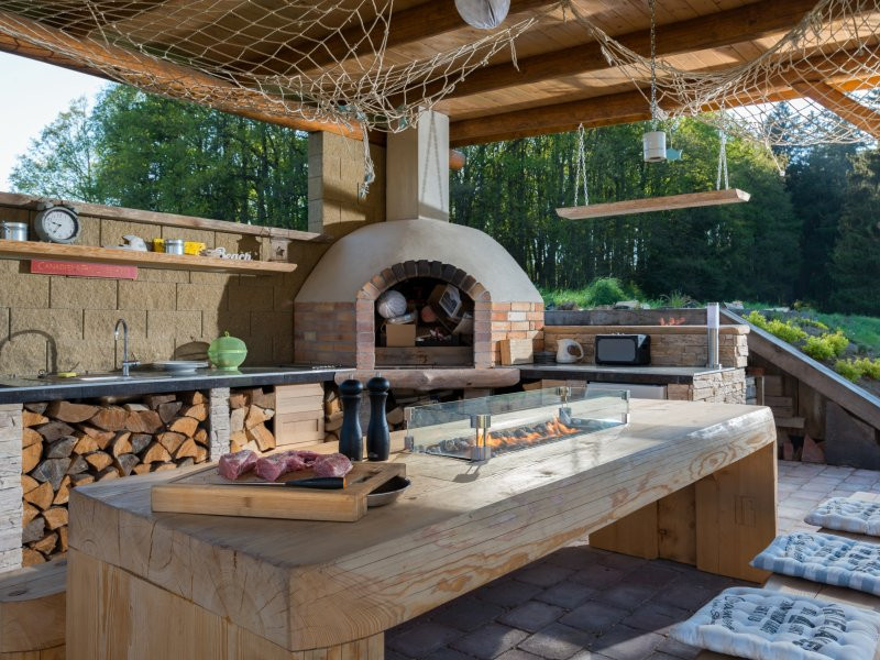 Zahradní kuchyně s masivním dřevěným stolem a živým ohněm